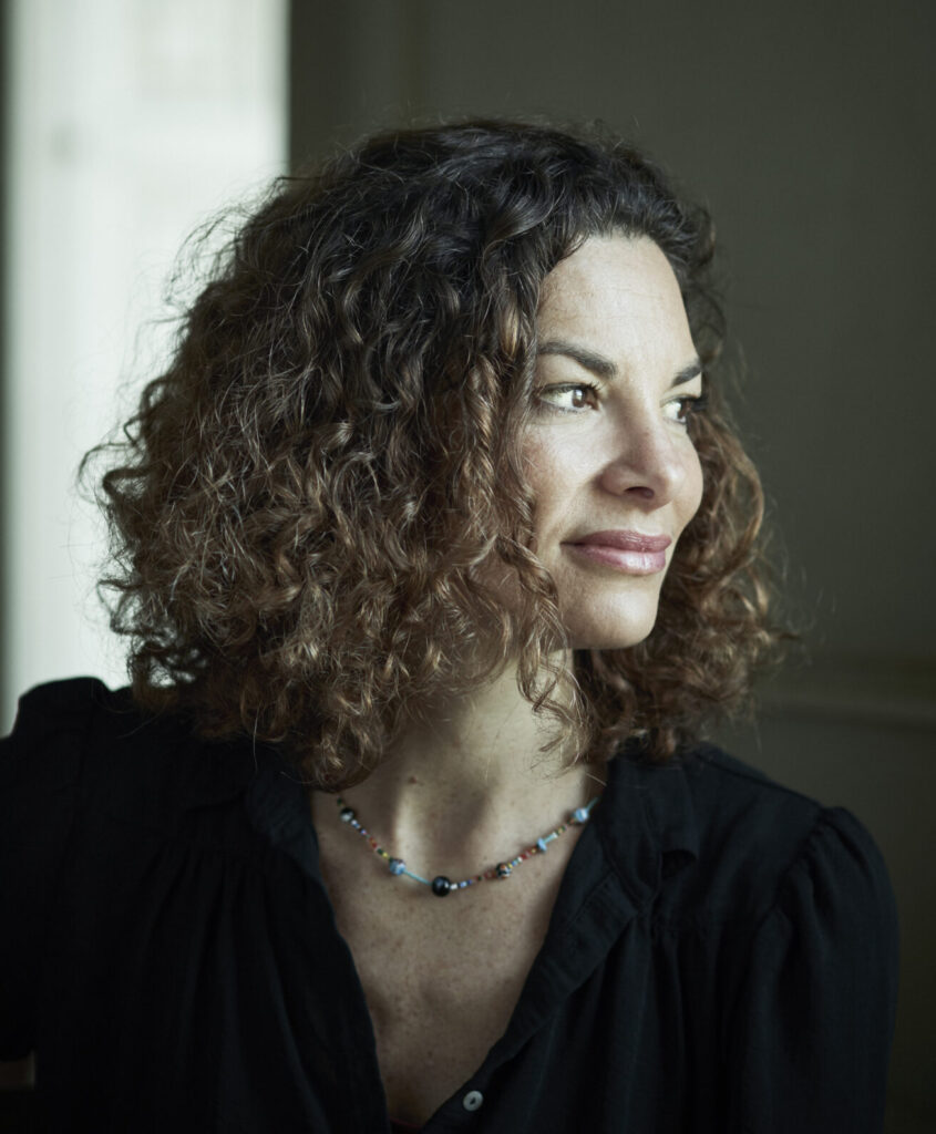 Portret van Gaia Vince, krullend bruin haar, zwarte blouse. Ze kijkt rechts het beeld uit.