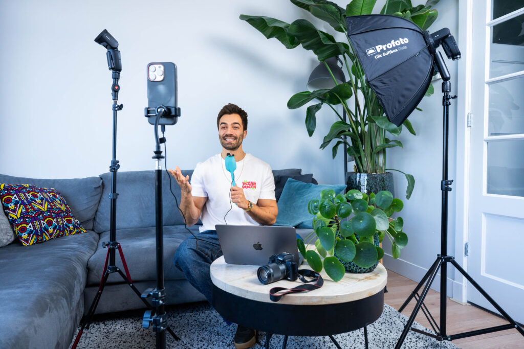 Dennis zit op een blauwe bank en praat geanimeerd in een microfoon. Om hem heen staan verschillende film lampen en zijn telefoon staat op een statief. Dennis heeft kort bruin haar, baard en snor. Hij draagt een wit t-shirt en een spijkerbroek.