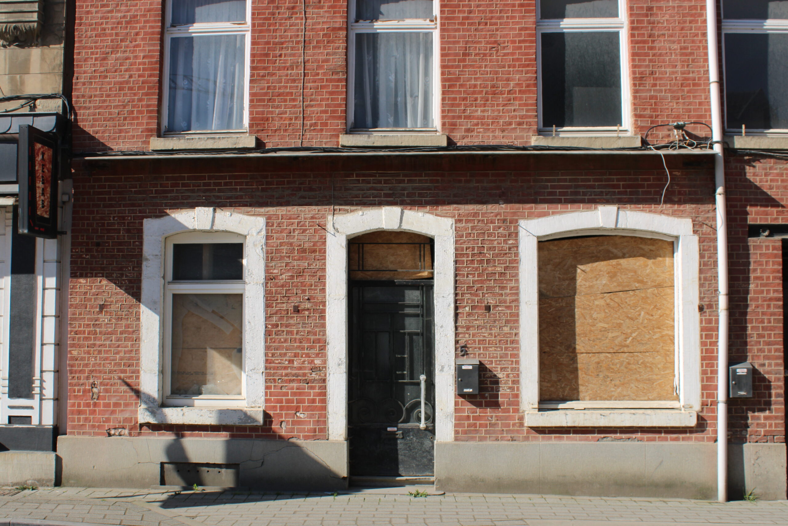 Een dichtgetimmerd huis in Limbourg. Een rode bakstenen gevel, met planken voor alle ramen. 