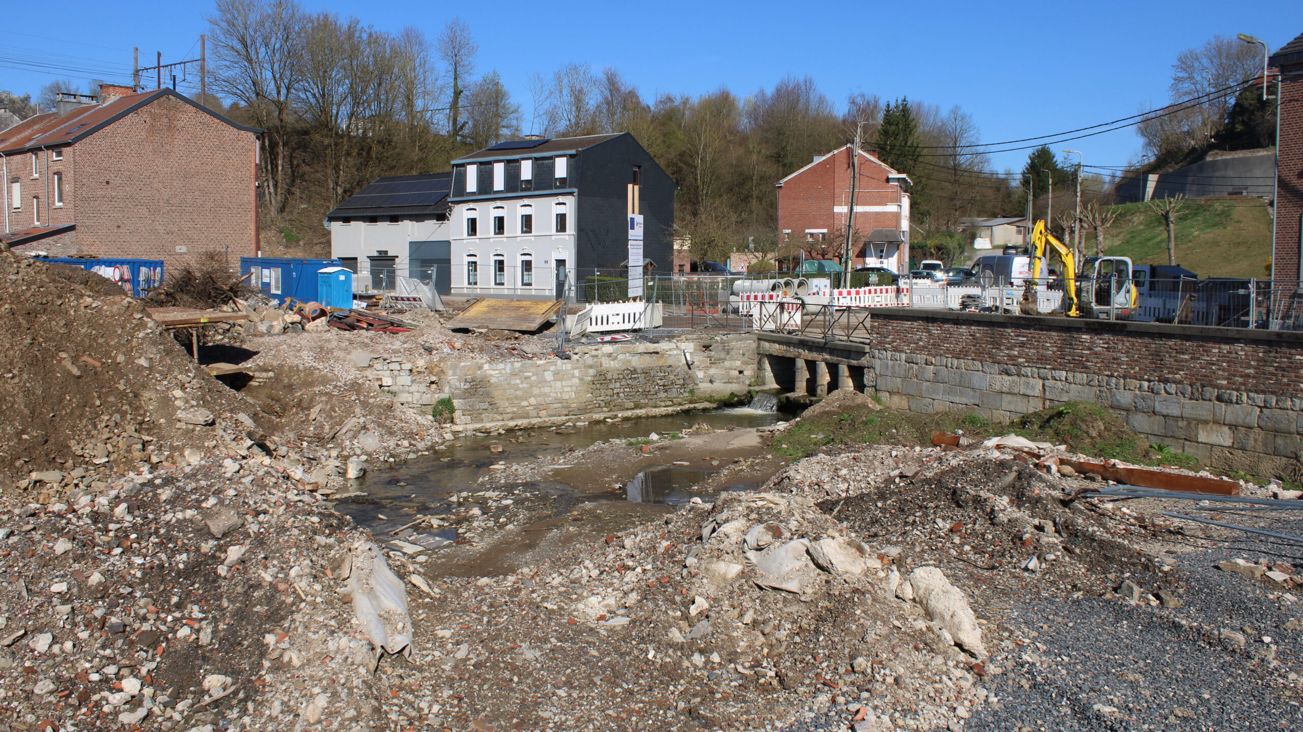 De schade langs de rivier. We zien het briggetje waar de rivier nu netjes onder door stroomt. Aan beide kanten liggen enorme hopen puin, alle begroeiing en bebouwing is weggeslagen. Op de achtergrond staan nog een paar huizen.