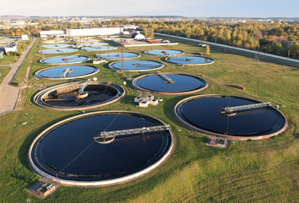Een rioolzuivering installatie van boven gezien: grote putten met water erin, meerdere rijen naast elkaar. Boven elke put loopt een loopbrug. 