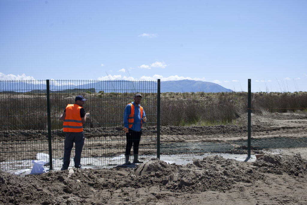 Bouw hekken midden in het natuurgebied.  De grond is hier platgewalst, een paar bouwvakkers in oranje hesjes staan bij de hekken.
